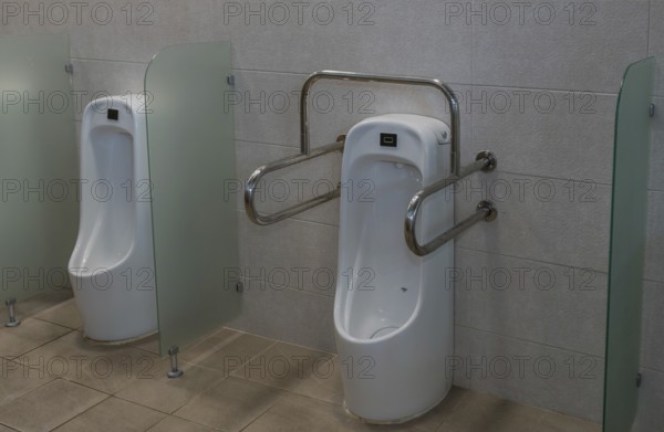 Porcelain urinal with handrails for use by disabled person next to non-disabled urinal in public