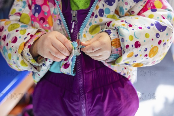 Close up shot on the hands of a kindergarten child struggling to latch and close the zipper of his