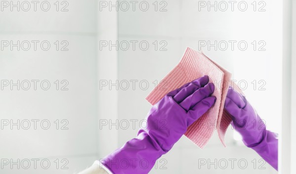 Cropped view of housekeeper woman hand in purple rubber gloves polishing mirror with pink cloth rag