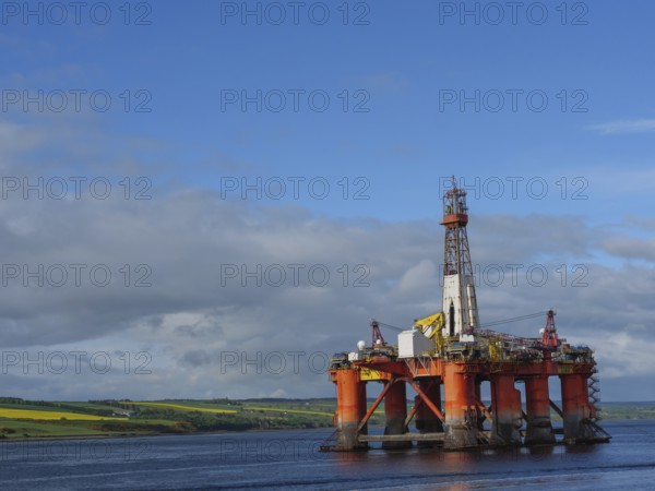 A single oil drilling platform sits in the calm sea with a slightly cloudy landscape behind it,