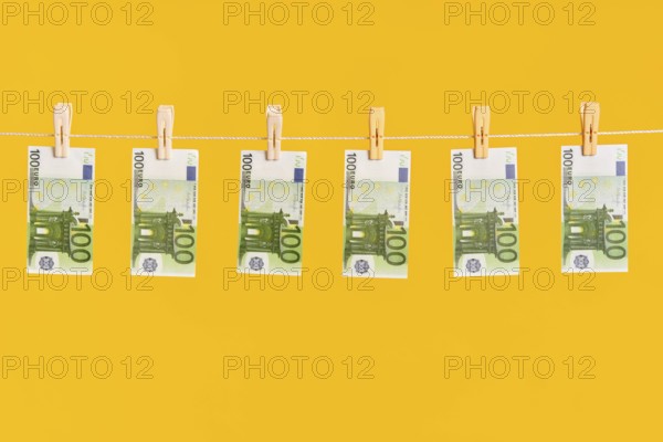 Money laundering, euro banknotes hanging on rope over yellow studio background. Finance,