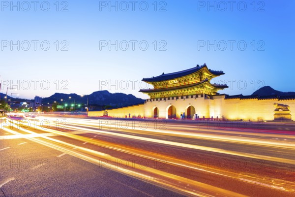 Colorful streaking headlights of cars passing in front of lighted gate of Gwanghuamun, entrance to