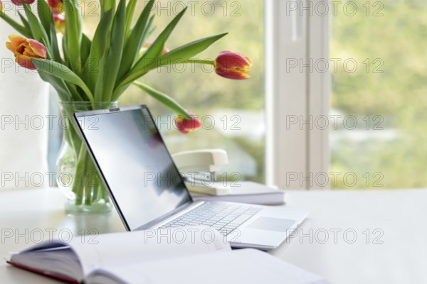 Laptop with organizer and a flower bouquet from tulips on a white desk by the window, business in