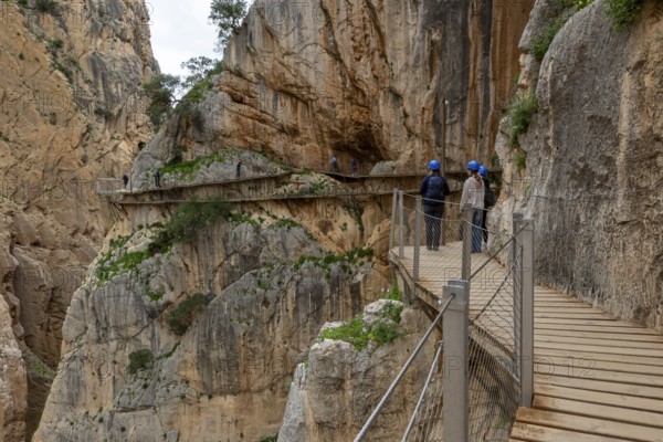 People with helmets walking on the wooden path Caminito del Rey along a rocky cliff, Malaga, Spain,