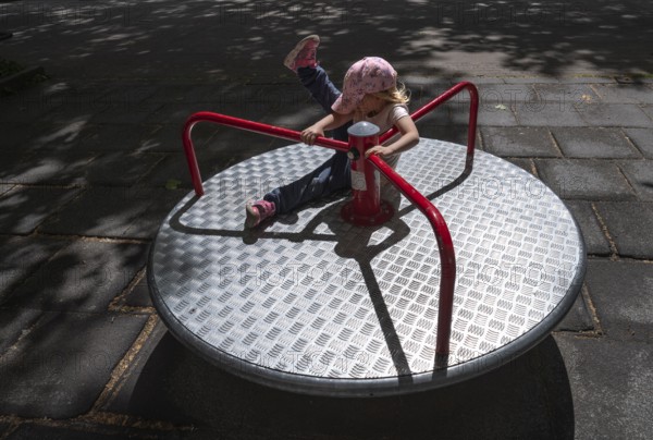 Outdoor shot, little girl, 3 years old, blonde, playing on a merry-go-round, children's playground,
