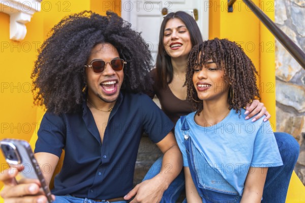 Three happy young friends are taking a selfie with a smartphone while sitting on the stairs of a