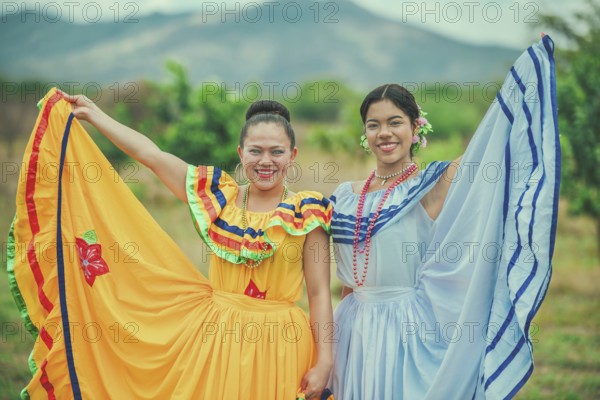 Portrait of two Hispanic women wearing cultural folkloric costume in a field. Two smiling Hispanic