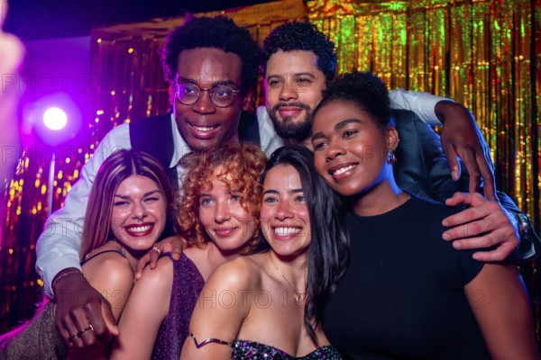 Group of cheerful elegant friends posing together for a photo at nightclub party with disco lights