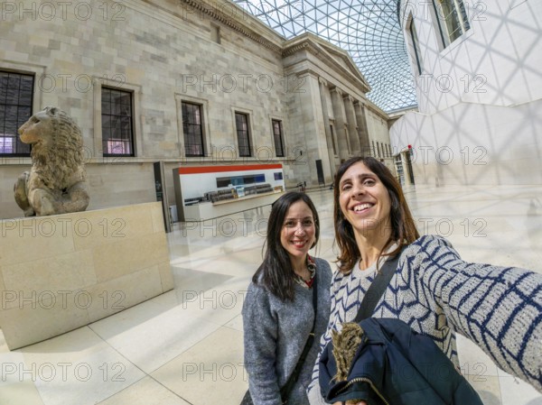 Two happy female tourists are taking a selfie with a fisheye lens at the british museum's great