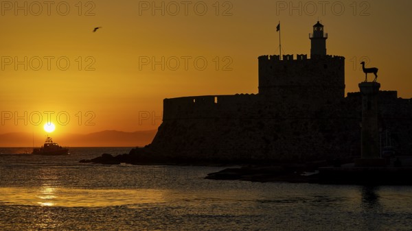 A boat glides in front of the silhouette of a fortress in the warm sunrise, dawn, Fort of Saint