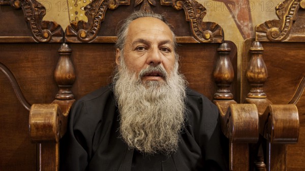 Portrait of a bearded man in black clothes, sitting on a wooden chair, Papas Nektarios, Monastery