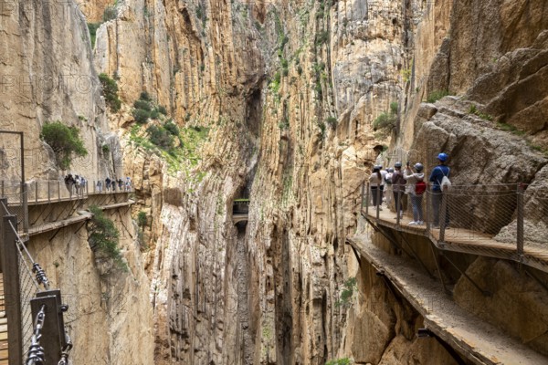 People with helmets walking along the Caminito del Rey in an impressive rocky landscape, Malaga,