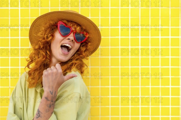 Cheerful influencer pointing her thumb while smiling, wearing a straw hat and heart shaped