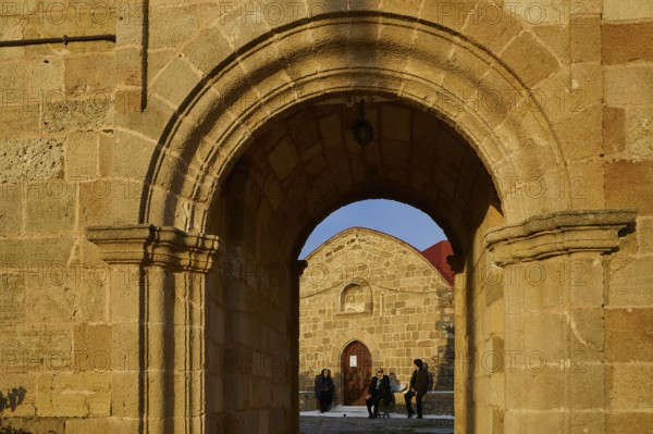 View through a stone arch onto people sitting and chatting in front of a church, Easter 2025,