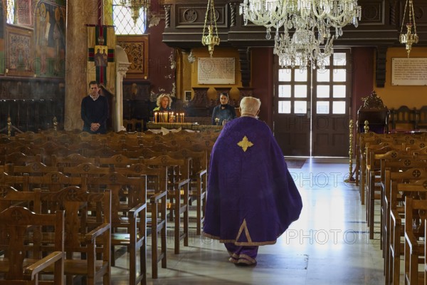 A priest in a purple robe walks through the empty pews of a church, Church of the Annunciation of