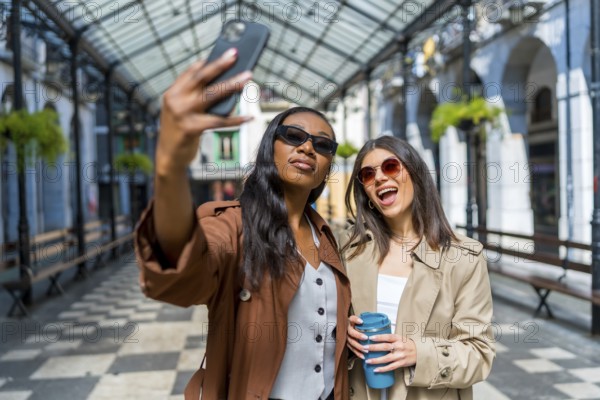 Two women are taking a selfie with a smartphone while walking down the street, holding reusable