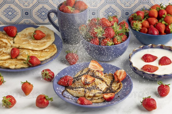 Icing sugar falls on pancakes with strawberries and chocolate syrup, fresh strawberries and yoghurt
