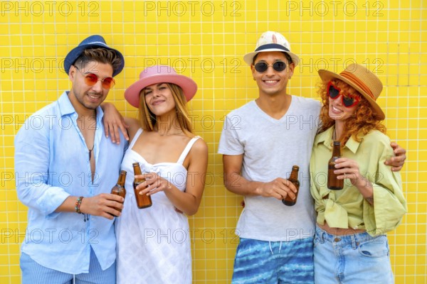 Four cheerful friends wearing summer clothes and hats are enjoying a refreshing beer against a