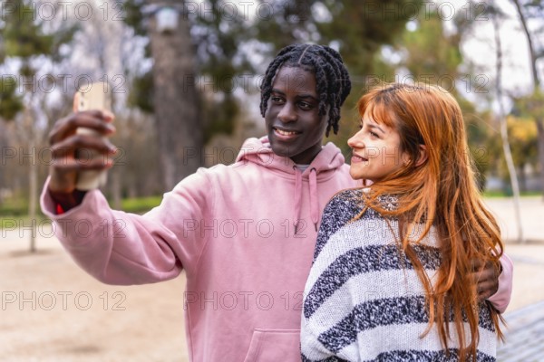 Young multiracial couple smiling together while capturing a joyful selfie with a smartphone in a