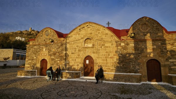 Stone church with rounded roofs and some people walking along in the evening light, Easter 2025,