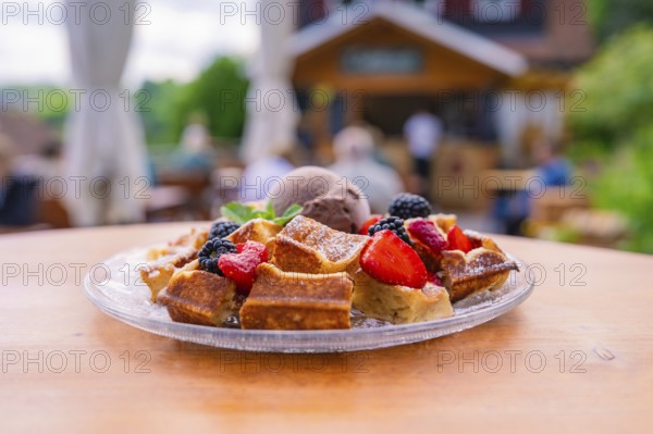 Fresh waffles with berries and ice cream on a table in front of a cosy outdoor café, Cafehäusle