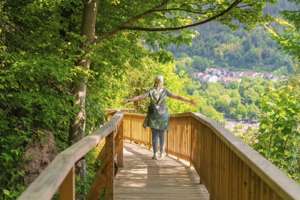 A person walks on a wooden path with outstretched arms through nature, Panorama Holzsteg, Calw,