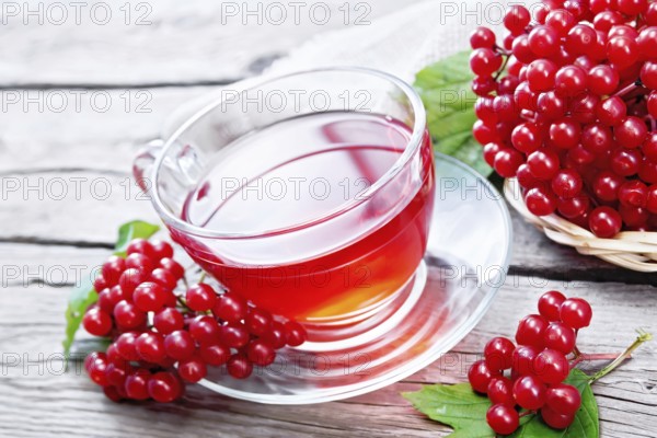 Tea with viburnum in a glass cup, green leaves, wicker plate with berries and burlap on wooden