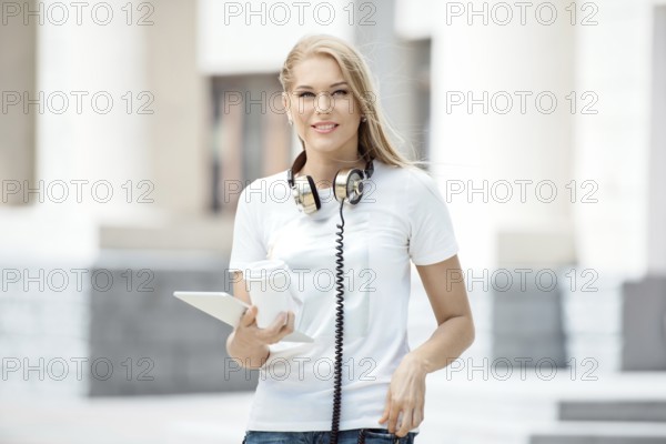 Happy young woman with vintage headphones around her neck, holding a cup of coffee to go and
