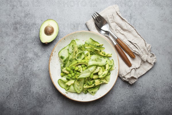 Healthy vegan green avocado salad bowl with sliced cucumbers, edamame beans, olive oil and herbs on