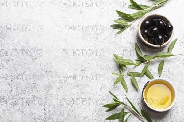 Black olives and extra virgin olive oil in little bowl with olive tree branches top view on white