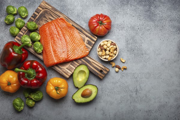 Fresh raw salmon fillet on wooden cutting board, organic bio vegetables and nuts on rustic stone