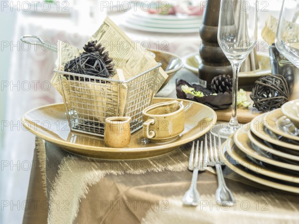 Set of new dishes on table with tablecloth. Stack of beige plates and wine glasses on restaurant