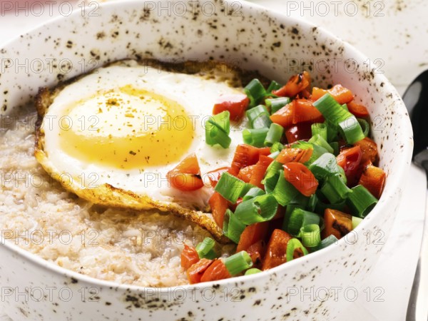 Savory oatmeal in craft trendy bowl, served with vegetables and fried egg on white concrete