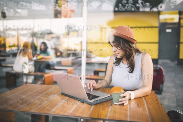 Beautiful young caucasian woman sitting on a terrace in a cafe in summer at a wooden table in a hat