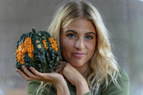 A stunning blonde model poses in a vibrant pumpkin field, wearing a stylish autumn outfit with a