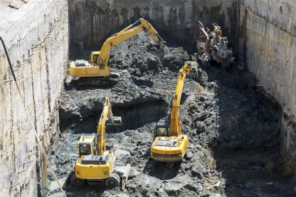 Excavators dig at a construction site of a street and a subway. Baggers transport dirt to a higher