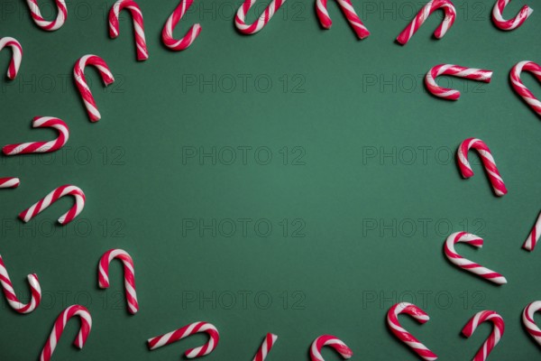Christmas sweets frame with mini candy canes in red and white stripes, on a green paper background