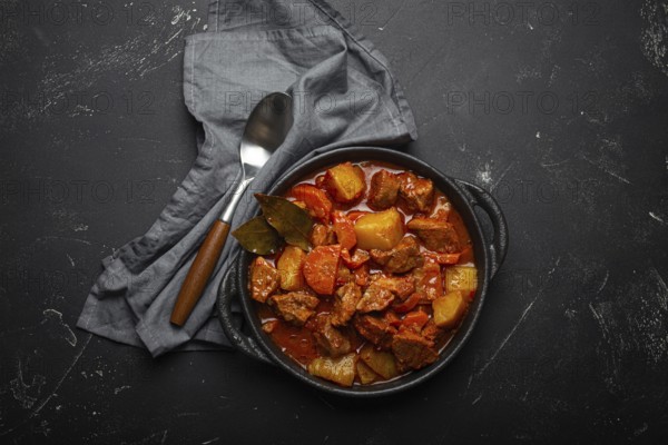 Beef meat stew with potatoes, carrot and delicious gravy in black casserole pot with bay leaves