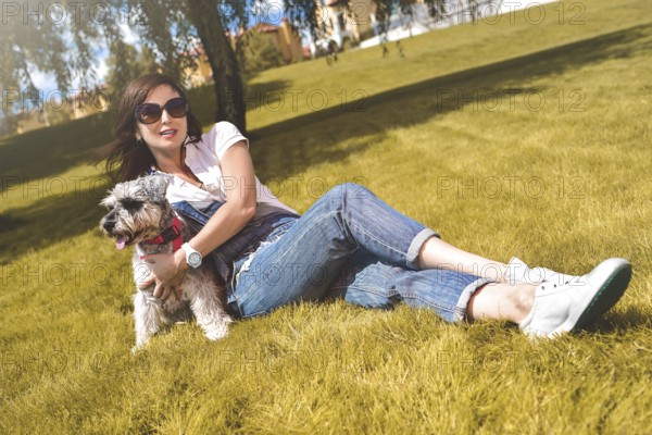 Pretty adult caucasian happy woman resting in the park on a sunny day with her beloved dog. Female