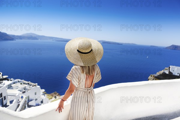 Young woman in a white dress and straw hat, walking at the city of Oia, island of Santorini, Greece