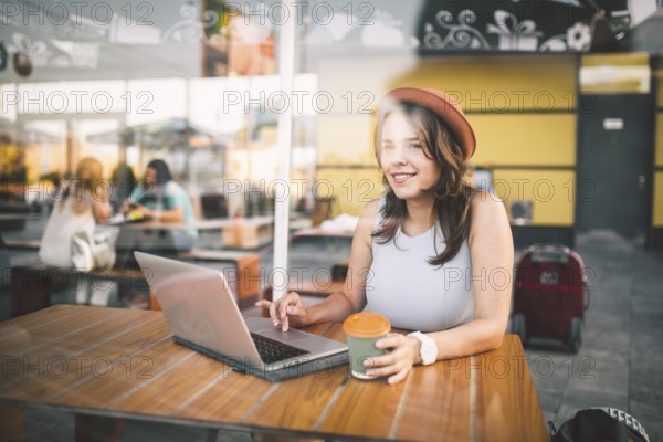 Beautiful young caucasian woman sitting on a terrace in a cafe in summer at a wooden table in a hat