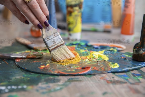 A detailed closeup of a hand skillfully mixing together vibrant and colorful paints on a palette