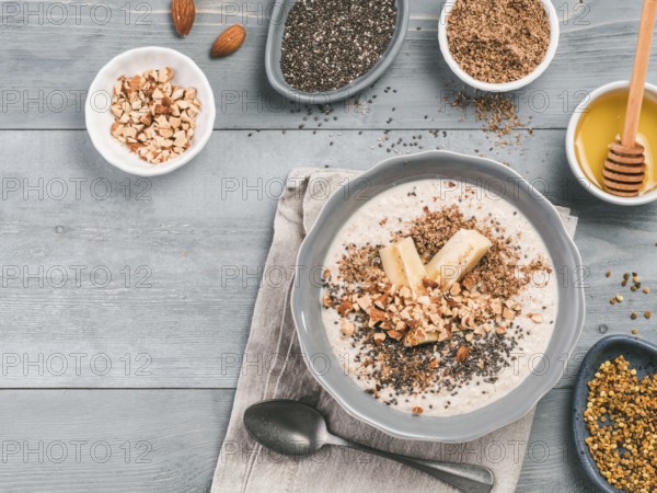 Overnight oats in bowl and ingredients - banana, LSA, chia seeds, almond, honey and pollen on gray
