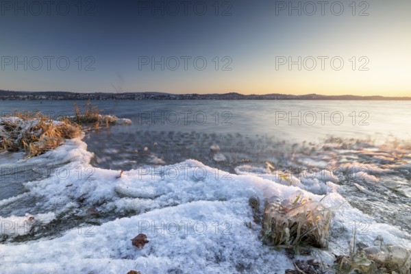 Snow-covered lakeshore with gentle waves at sunrise, Niederzell, Reichenau, Lake Constance,