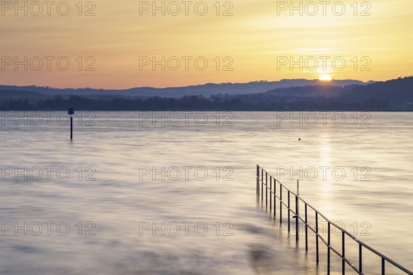Sunrise over a calm lake with railings and distant hills, lido, Litzelstetten, Lake Constance,