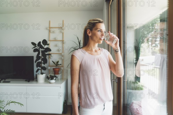 Smiling young caucasian woman taking her morning supplements, vitamin pills with a glass of water