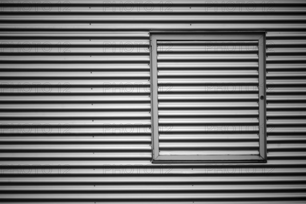 Close-up of the corrugated sheet metal façade of an industrial building with a metal window frame