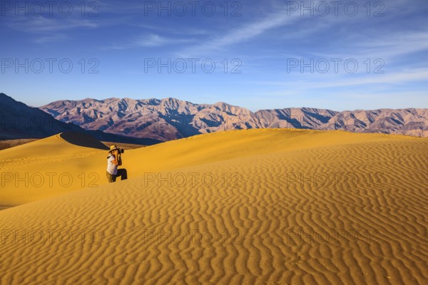 Woman in striped shirt and straw hat photographing sand waves. Bright morning in picturesque part