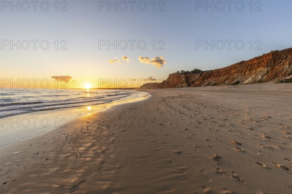 Beautiful sandy beach with red rocks and cliffs. Twilight at sunset with shallow waves on the