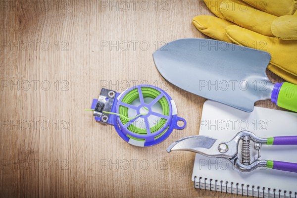 Protective gloves pruning shears garden tie wire hand shovel notepad on wooden board gardening